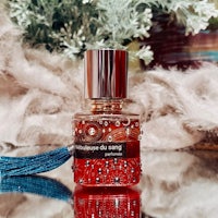 a bottle of red perfume with a blue tassel on it