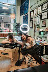 two women sitting at a table in a tattoo shop