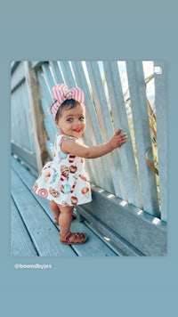 an image of a baby girl leaning against a fence