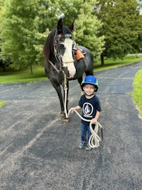 a young boy standing next to a horse with a rope