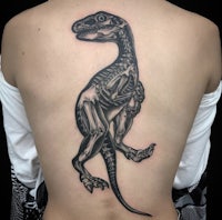 the back of a woman with a t - rex skeleton tattoo