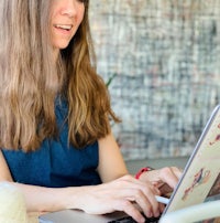 a woman with long hair sitting at a table with a laptop