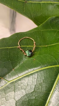 a ring with a green stone on top of a leaf