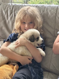 a little girl holding a white puppy on a couch