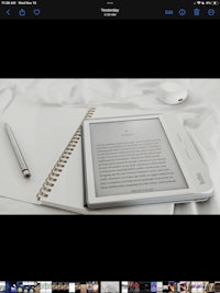 a kindle e-reader on a bed with a pen on it