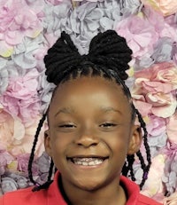 a young girl with dreadlocks smiling in front of a flower wall