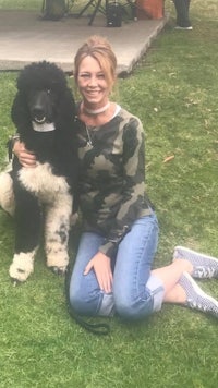 a woman in a camouflage shirt with a black poodle