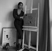 a black and white photo of a woman standing next to an easel