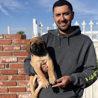 a man holding a puppy in front of a brick wall