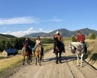 a group of people riding horses on a dirt road