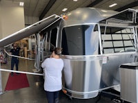 a woman is standing next to a silver airstream trailer