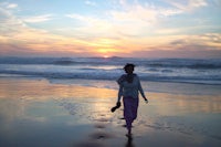 a woman walking on a beach at sunset