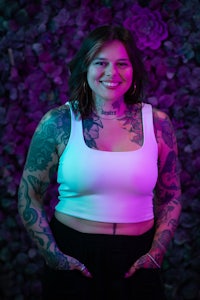 a woman with tattoos standing in front of a purple wall