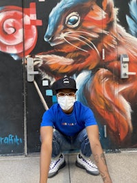 a man crouching in front of a mural with a squirrel and a lollipop