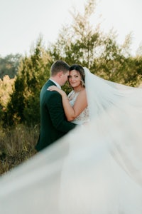 a bride and groom embracing in a field with a veil