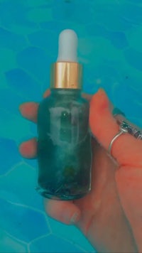 a person holding a bottle of oil next to a pool
