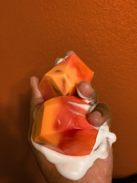 a hand holding a piece of orange and cream soap
