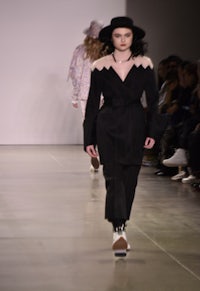 a model walks down a runway wearing a black coat and hat