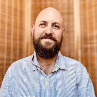 a bald man with a beard in front of a wooden wall