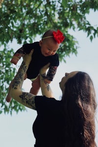 a woman holding a baby up in the air with tattoos