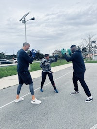 three people practicing boxing in a parking lot