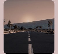 an empty road with the sun setting behind it
