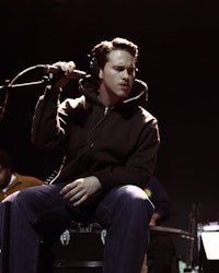 a man in a black hoodie sitting on a stool