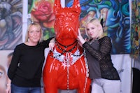 two women standing next to a red dog statue