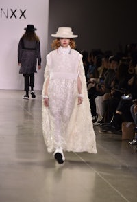 a model walks down the runway in a white dress and hat