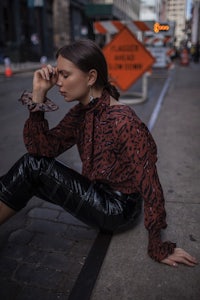 a woman sitting on the sidewalk in a leopard print top and leather pants