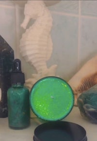 a bottle of green glitter soap and seashells on a counter