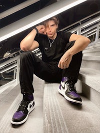 a man sitting on a set of stairs wearing purple and black sneakers