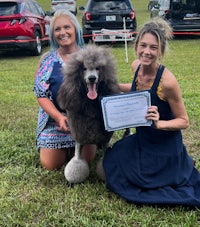 two women posing with a poodle and a certificate
