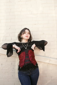 a woman in a red corset leaning against a brick wall