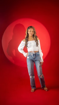 a young woman in jeans and a white top posing in front of a red background