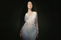 a woman in a white dress posing in front of a dark background