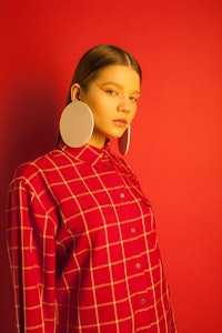 a woman wearing a red plaid shirt and ear studs on a red background