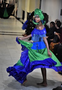 a woman in a blue and green dress walking down the runway