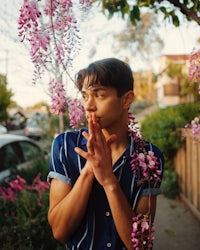 a young man posing in front of a flowering tree