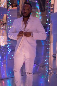 a man in a white suit standing in a room with lights