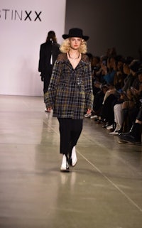 a model walks down the runway wearing a hat and coat