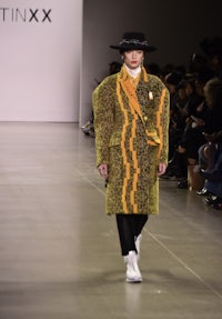 a model walks down the runway wearing a yellow coat and hat