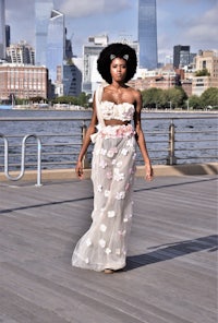 a black woman in a floral dress walking on a boardwalk with a view of the city