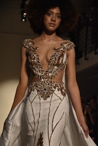 a model walks down the runway in a white and gold gown