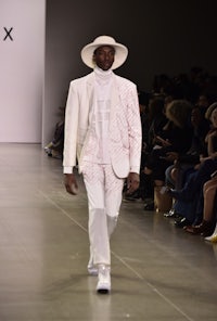 a man walking down the runway in a white suit and hat