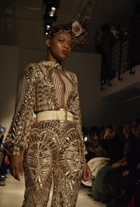 a woman in a gold outfit walks down the runway