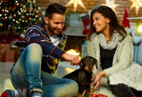a young couple with a dog sitting on the floor in front of a christmas tree