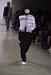 a model walks down the runway wearing a hat and jacket