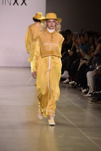 a woman walking down the runway in a yellow dress and hat