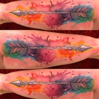 an arrow tattoo with watercolor splatters on it